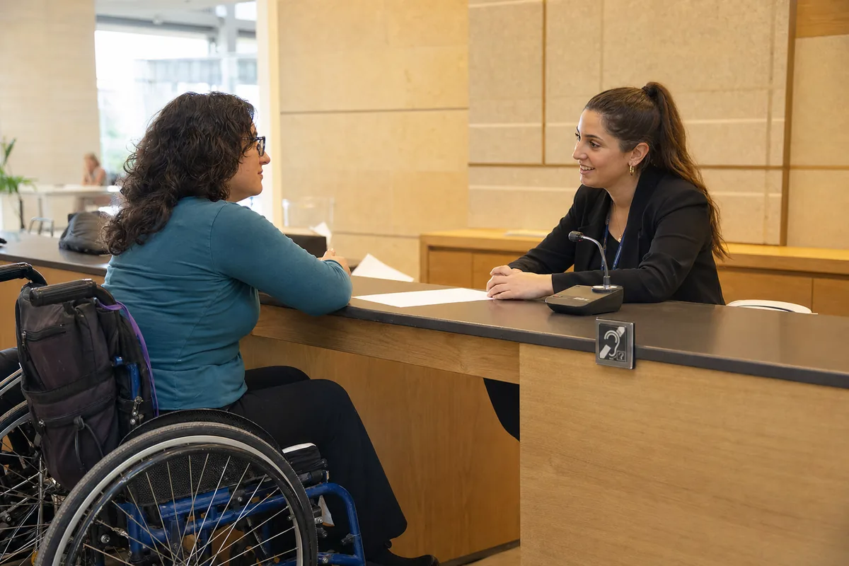 לקוחה יושבת מקבלת שירות בדלפק נגיש עם משטח פנוי ומערכת עזר לשמיעה